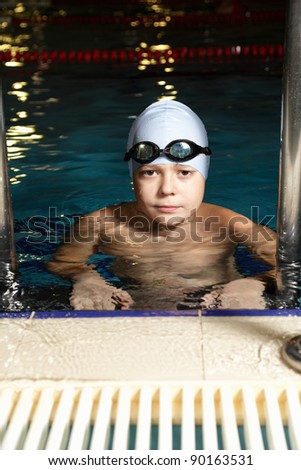 Boy in goggles at swimming pool edge holding stair