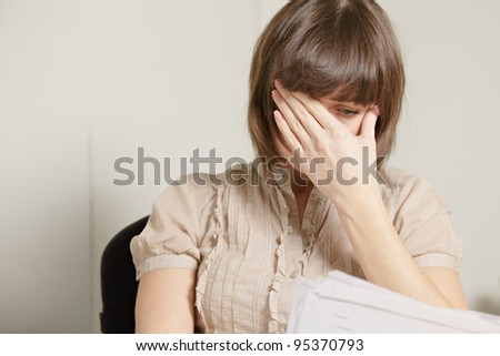 Young brunette woman reading report covering face with palm