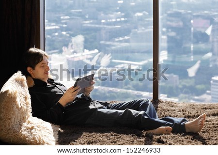 Young man on couch with tablet against big window