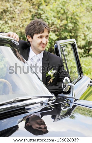 Smiling groom at the black car looking sideways