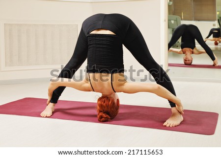 Redhead in standing on a head yoga pose looking at own reflection