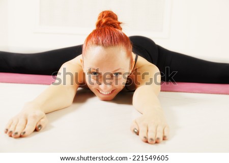 Smiling redhead exercising yoga laying down on floor legs stretched closeup