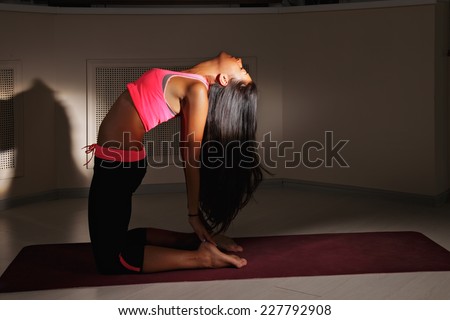 Young brunette woman bending back while exercising yoga in darkness