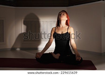 Redhead taking deep breath while meditating in a dark gym