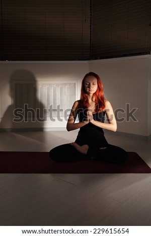 Redhead woman meditating in lotus yoga pose with eyes closed and palms folded at face