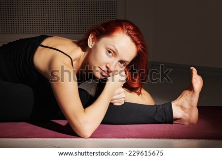 Serene redhead yoga trainer leaning on hands while sitting in split pose