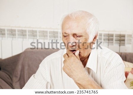 Old man wearing white shirt in thoughts sitting on the sofa