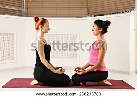 Two women relaxing in yoga class while sitting in front of each other on the red mat