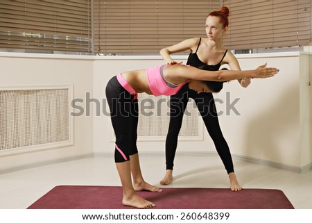 Instructor keeping student\'s back flat while exercising yoga in gym