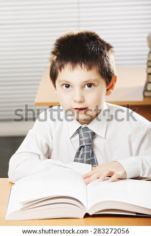 Caucasian kid with book talking while sitting at the desk in classroom