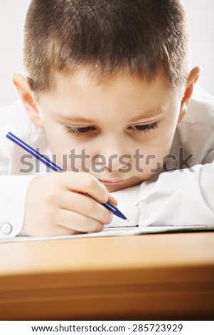Caucasian schoolboy wearing formal school wear writing at the desk closeup
