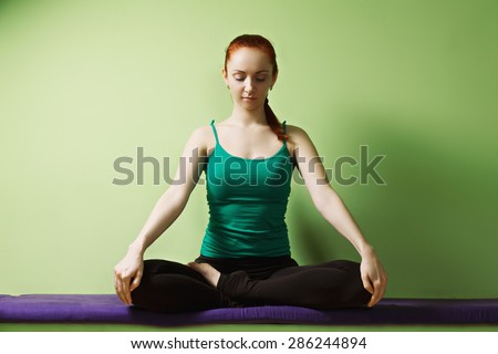 Relaxed redhead caucasian woman meditatind in lotus yoga position at the green wall