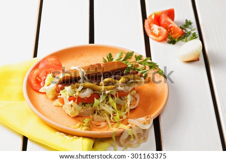 Hotdog on plate with iceberg lettuce, onions and tomatoes over white wooden tabletop