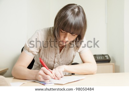 Young brunette woman writing on paper sheet at office desk
