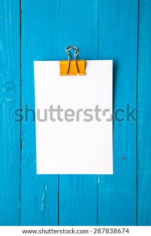 blank sheet of paper with a clip on a blue wooden background