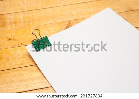 sheets of paper in a green metal clips on a wooden background