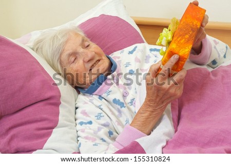 Happy elderly woman holding a present in the bed