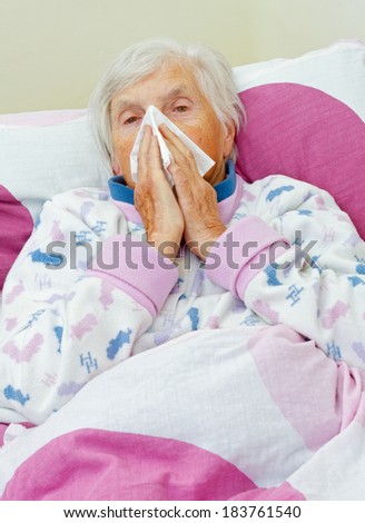 Elderly woman blowing her nose in the bed