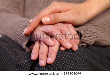 Nurse\'s hand comforting an elderly woman\'s wrinkled hand.