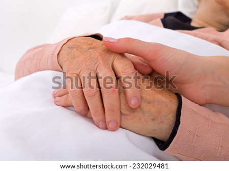 Caregiver holding elderly patients hand at home
