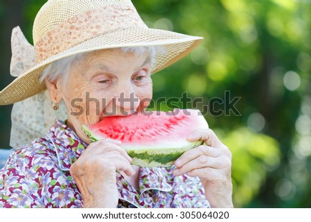 Happy elderly woman eating watermelon in the garden