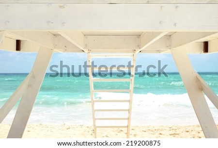 White Lifeguard house on a sandy beach in summer with turquoise ocean and blue cloudy sky