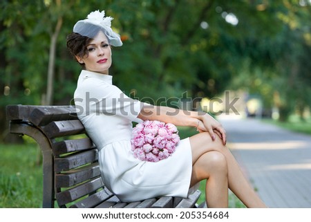 Beautiful bride in stylish sheath dress with bouquet of peony flowers on the bench. Wedding.