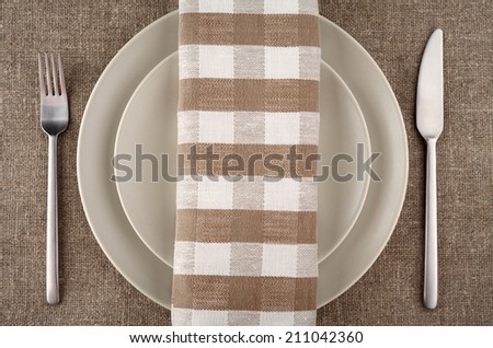 Table setting. Beige plate, fork, knife and beige linen napkin and tablecloth.