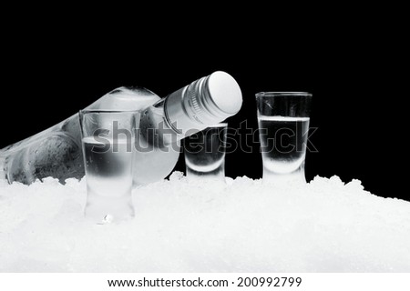 Studio shot of bottle with glasses of vodka lying on ice on black background