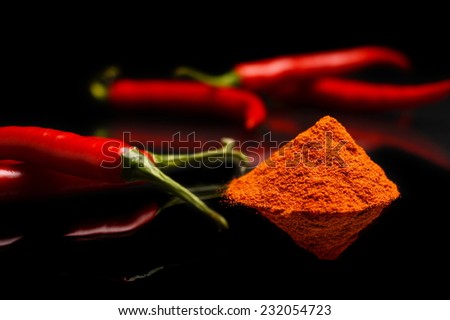 Studio shot of spicy chilli peppers and stack of cayenne pepper isolated on black background