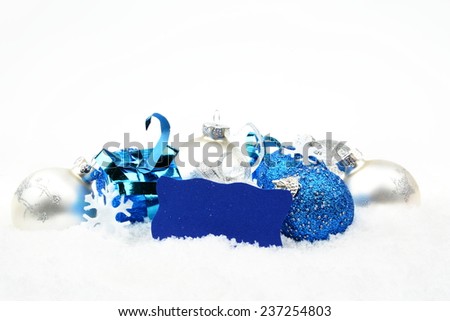 Decoration of silver and blue christmas baubles and gifts with wishes card on snow white background