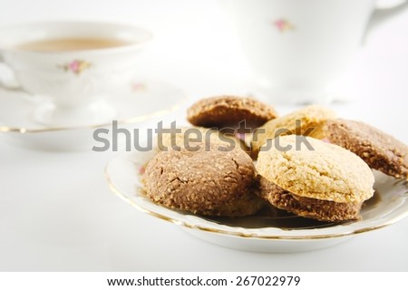 Old-style porcelain kettle with cup of tea with cookies foreground on white background