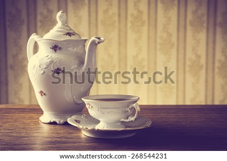 Old-fashioned porcelain jug with a cup of tea with old-fashioned wallpaper background