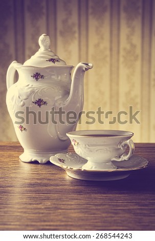Old-fashioned porcelain jug with a cup of tea with old-fashioned wallpaper background