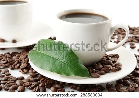 Scattered coffee beans with cups of coffee and green coffee leaf