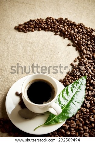 Scattered coffee beans twisted in a swirl with cup on fabric linen with green leaf