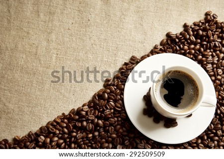Closeup scattered coffee cup with foam and plenty beans in the corner fabric linen