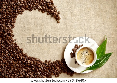 Scattered coffee beans twisted in a swirl with coffee cup with foam on fabric linen with green leaf