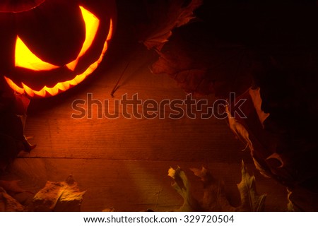 Scary halloween night with spooky evil face of jack o lantern in the corner with red shadows on the wooden surface