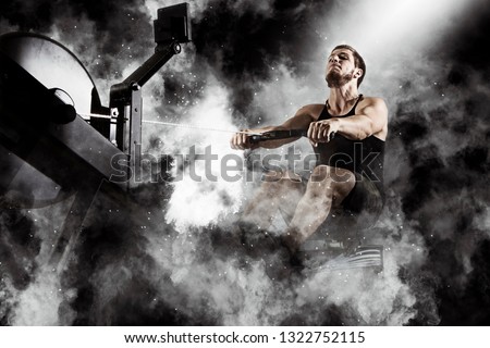 Bearded fit man using rowing machine at functional training gym