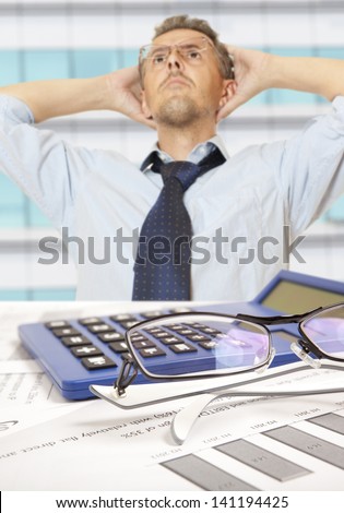 Accountant at desk in shirt and tie holding his head