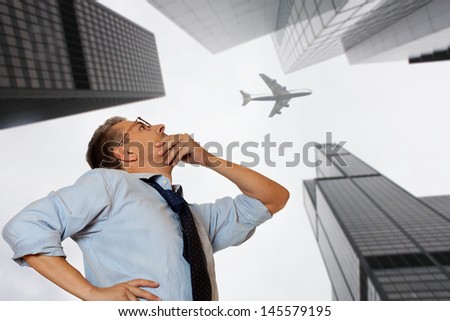 Businessman looking at a skyscraper and flying plane
