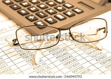 Glasses and calculator on paper table with finance report. Sepia color