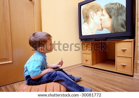 Rear view of little boy sitting on the floor and watching cinema  on TV at home