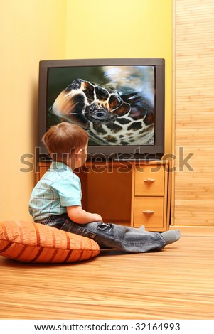 Rear view of little boy sitting on the floor and watching cinema on TV at home. TV screen - \