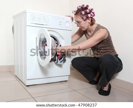 The woman with hair curlers adds garment to washing machine