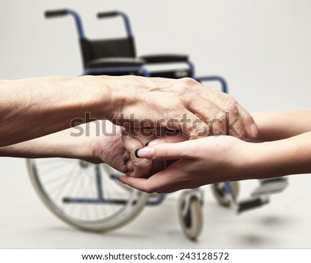 Hands of an elderly man holding the hand of a younger woman on wheelchair background