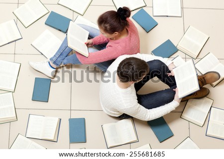 Young woman and man reading a book, top view. Blurred text is unreadable