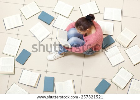 Girl reading a book, top view. Blurred text is unreadable