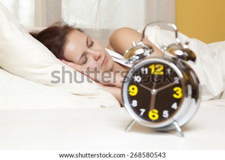 Sleeping woman resting in bed with alarm clock ready to wake her in the morning